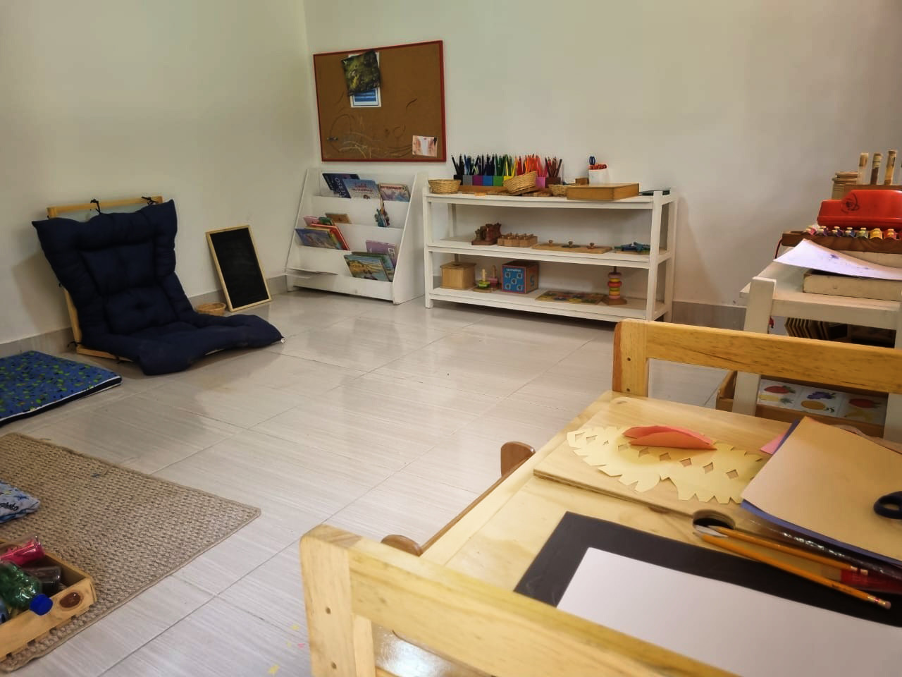 Ambiente preparado interior con estanterías bajas, libros, materiales y mesas a escala infantil.