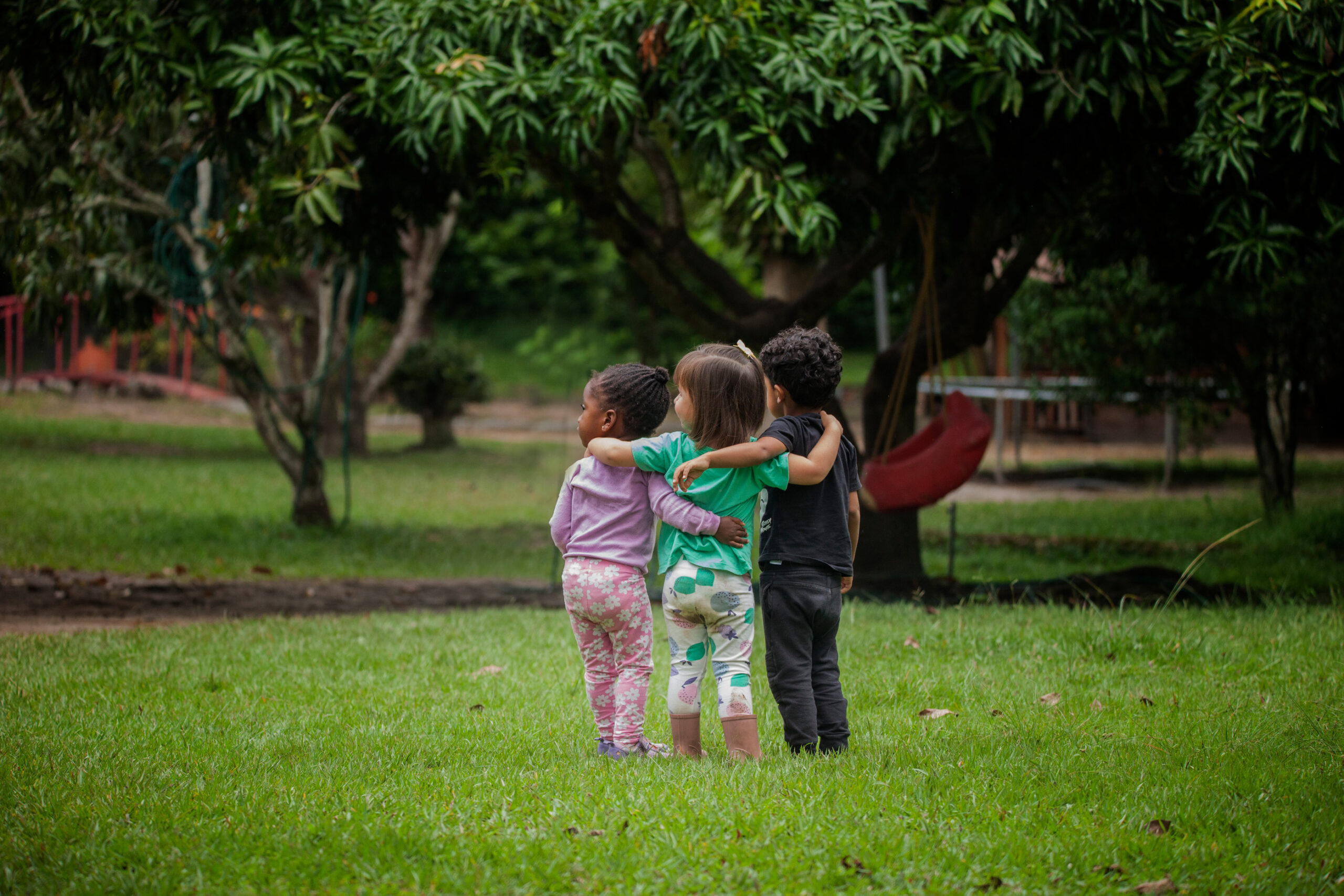 Tres estudiantes de primeros años caminan abrazados por una zona verde de Colibrí.