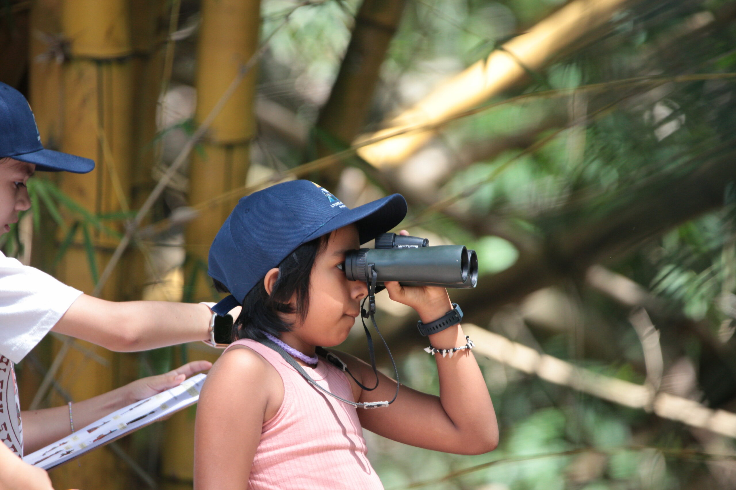 Estudiante observa el entorno natural con binoculares durante una exploración al aire libre.